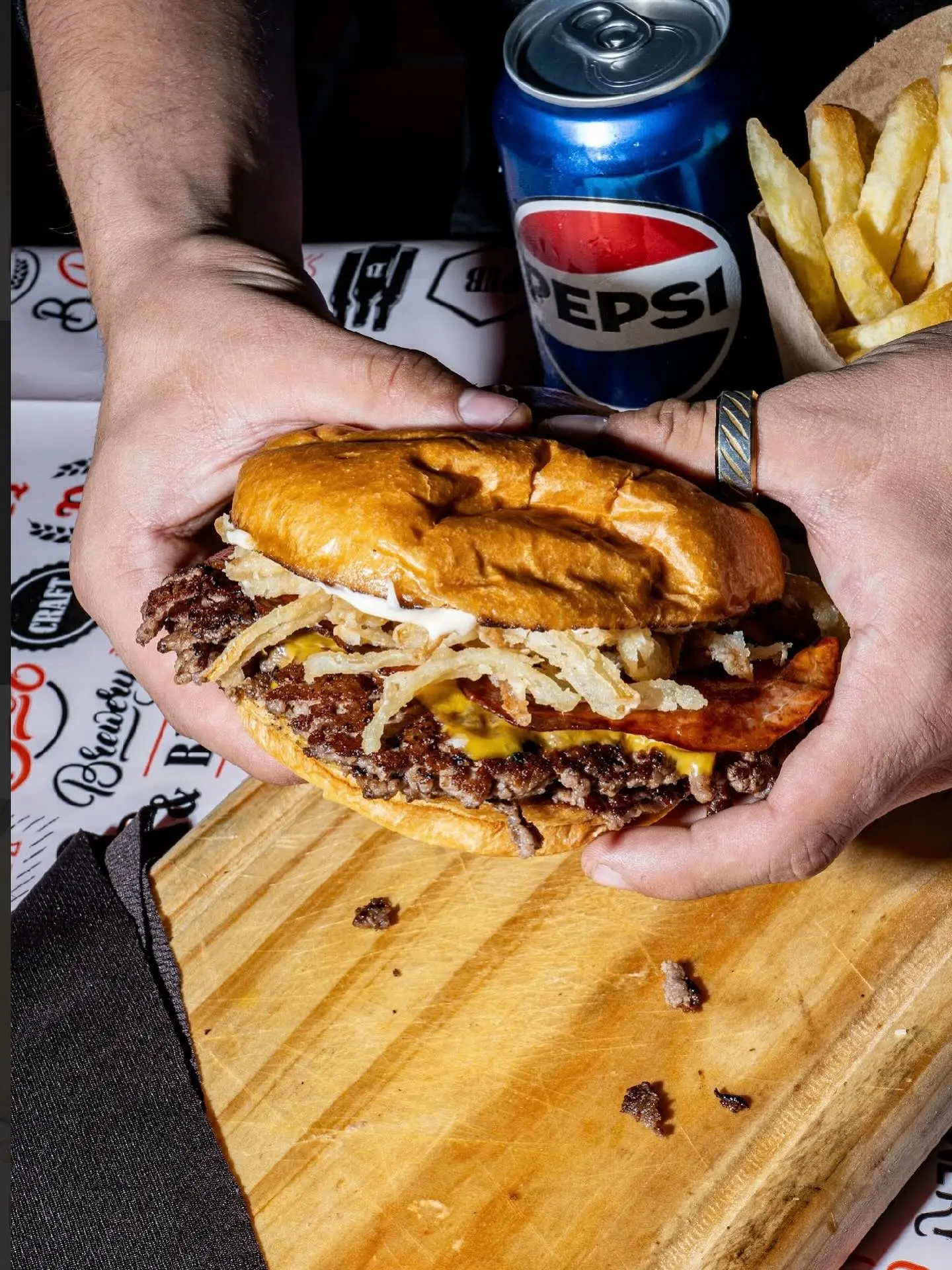 Smash burger con aros de cebolla crispy junto a una lata de Pepsi y papas fritas